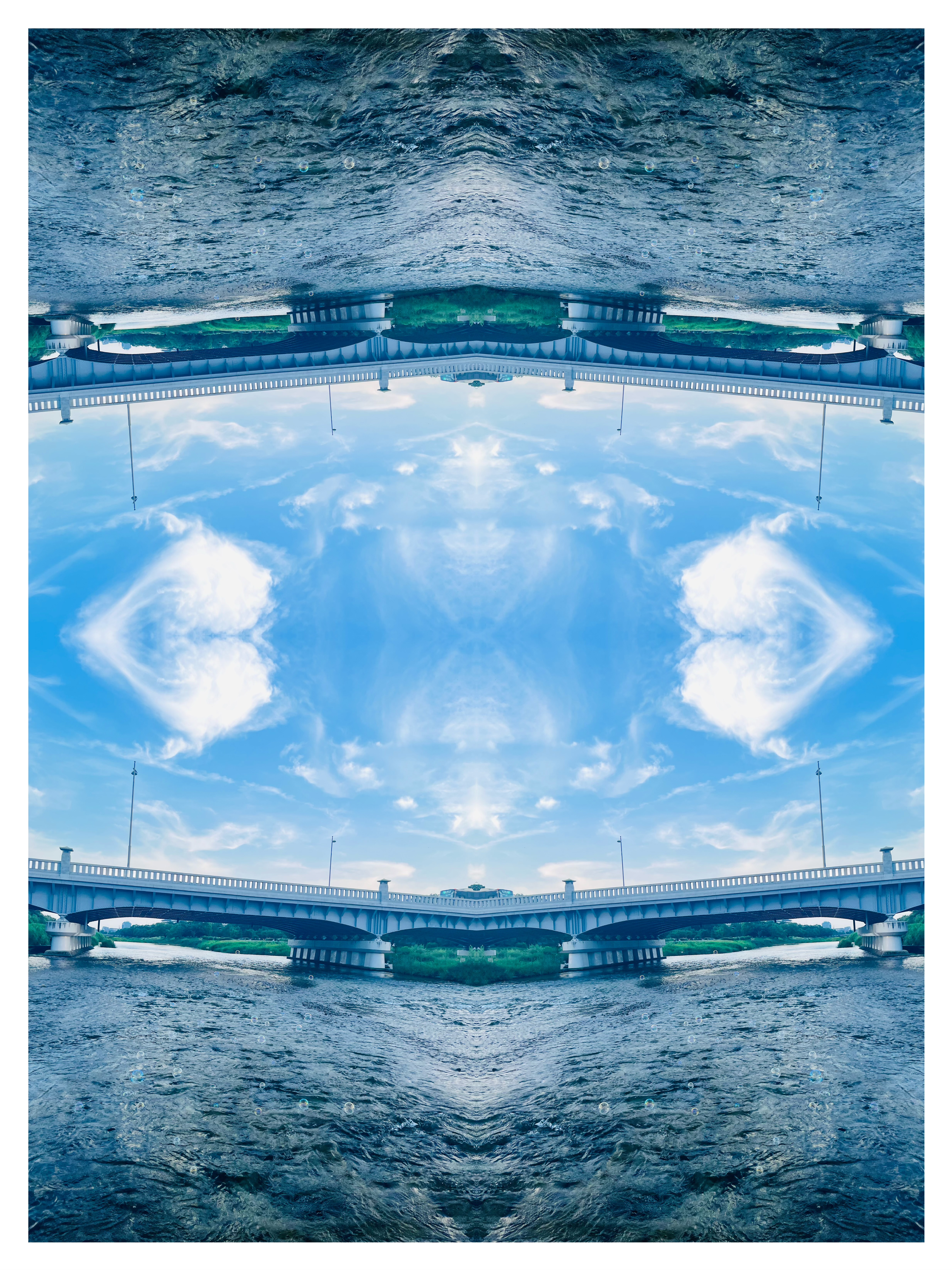 鴨川の川と橋を上下反転させ、橋の構造が中央で砂時計のような形を生み出し、青空に浮かぶ雲がハート型に見える対称構図の反転写真作品
