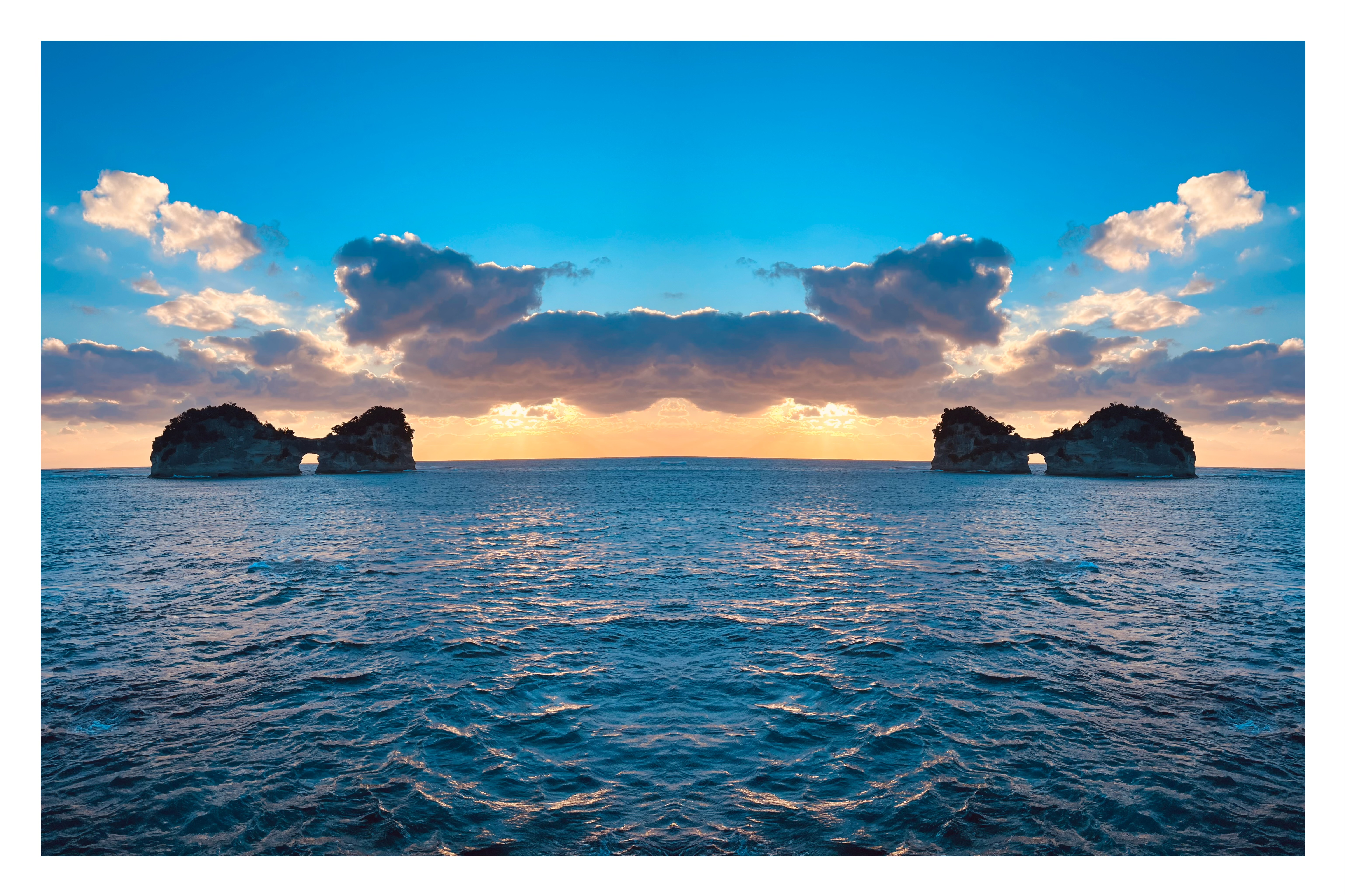 夕暮れの海に浮かぶ円月島を左右反転し、2つの島が向かい合うように配置された群青色の空と海が広がる反転写真作品